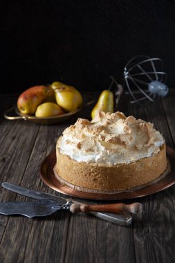 Sonbahar hala hayattır. Kaba ahşap bir masanın üzerinde taze pişmiş kremalı bisküviyle birlikte bakır bir tabak var. Pasta ve bıçak için bir spatulaya yakın. Arka planda olgun armutlar ve bir çırpı var..