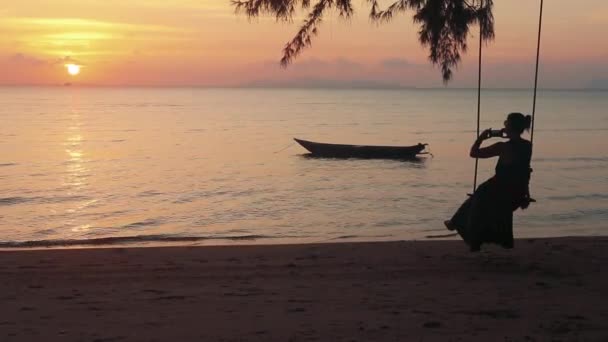 快乐女人摇摆在摇摆和拍摄她的手机日落海滩 — 图库视频影像