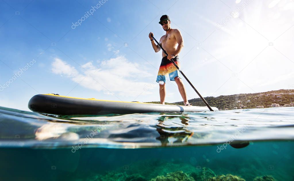 Young man on paddleboard, half under and half above water composition. Paddleboarding is the modern way of transportation and water activity sport.