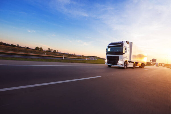 Loaded European truck on motorway in beautiful sunset light. On the road transportation and cargo.