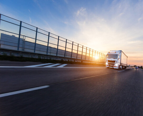 Loaded European truck on motorway in beautiful sunset light. On the road transportation and cargo.