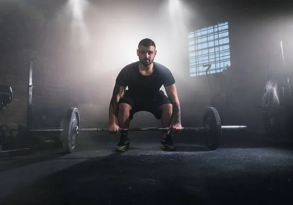 Weightlifter flipping two-handed dumbbell and preparing for workout in gym interior. Cinematic mood with dust, dramatic lightning and smoke. Active and healthy lifestyle.