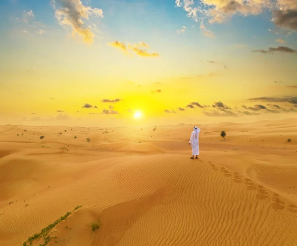 アラビア人が砂漠で日没時に歩いています 伝統的なアラビアのスーツに身を包んだ — ストック写真