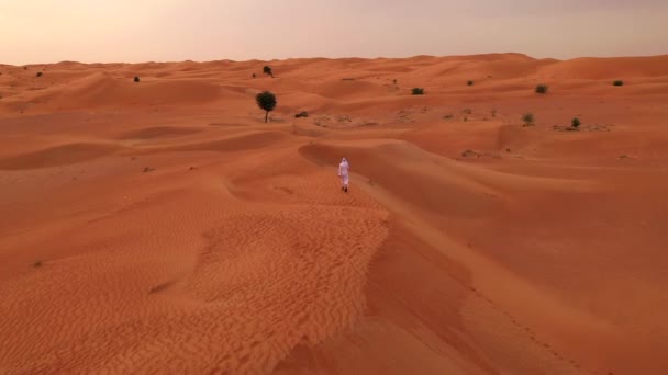 砂漠の砂丘を歩いて伝統的な服を着るアラビア人の空中映像 — ストック動画
