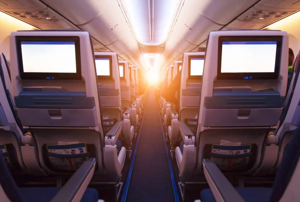 Airplane interior with row seats and blank touch entertainment screens. Concept of fast travel and new technologies.
