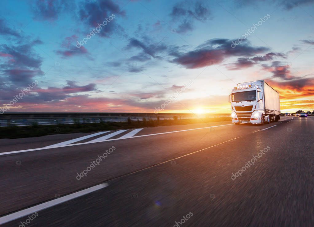 Loaded European truck on motorway in beautiful sunset light. On the road transportation and cargo.
