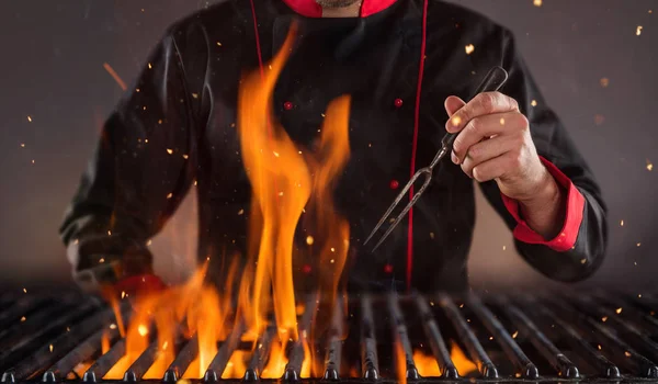 Zbliżenie kucharz trzyma widelec nad grill — Zdjęcie stockowe