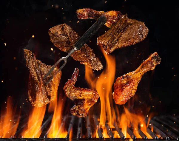 Flying beef steaks and chicken pieces above grill — Stock Photo, Image