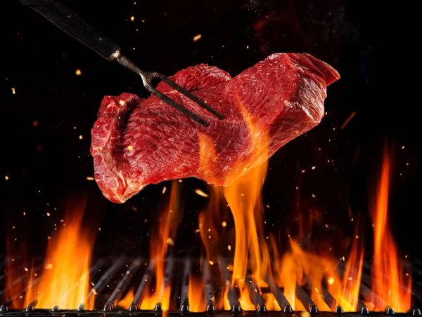 Flying raw beef steak above burning grill grid — Stock Photo, Image