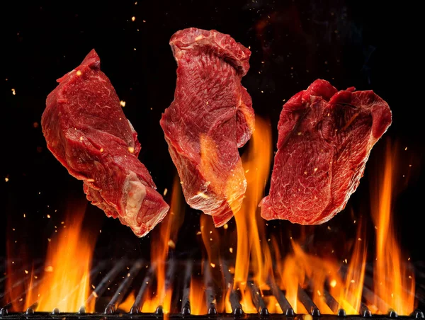 Bifes de carne crua voadores acima da grelha de grelha em chamas — Fotografia de Stock