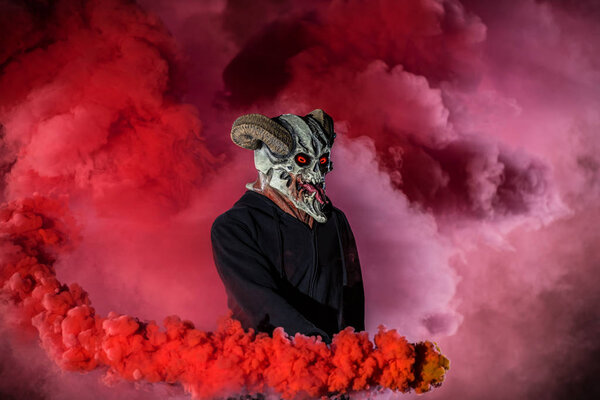 Devil with scary mask surrounded by red smoke