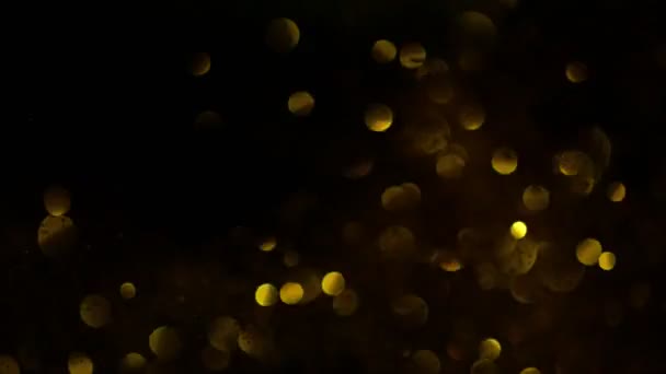 Mouvement super lent de particules dorées scintillantes sur fond noir. Faible profondeur de mise au point. Filmé sur caméra de cinéma à grande vitesse, 1000 images par seconde.