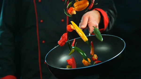 Keittiömestarin lähikuva paistamisesta putoavilla chili-paprikoilla — kuvapankkivalokuva