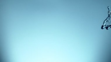 Uçan suyun yumuşak mavi arka planda çok yavaş sıçraması. Yüksek hızlı sinema kamerası, 1000fps.