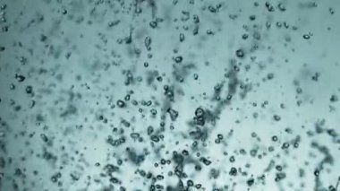 Uçan suyun yumuşak mavi arka planda çok yavaş sıçraması. Yüksek hızlı sinema kamerası, 1000fps.