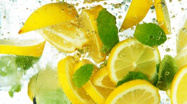 Limon dilimleri buz küpleri ve yapraklar, beyaz arka planda izole bir şekilde suyun altına düşüyor.