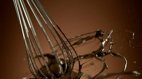 柔らかいグラデーションの背景に隔離されたホット溶かしたチョコレートを回転ワイヤー泡立て器の凍結運動 — ストック写真