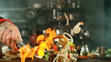 Wok Pan 'ın Dondurucu Hareketi ve Uçan Malzemeler. Şef Tuz Dökme. Arka plandaki Mutfak.