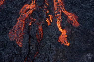 Parlak turuncu çatlakları ve desenli yüzeyi olan parlak erimiş lavın yakın plan çekimi..