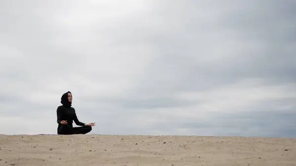 Muslim woman in hijab exercising healthy lifestyle yoga exercise in desert at sunset