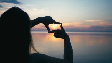 El ile çerçeve hale neşeli genç kadın. Kadın parmakları ile yapılan hayali kamera üzerinden seyir portresi. Yaz tatili sırasında çekici Bayan