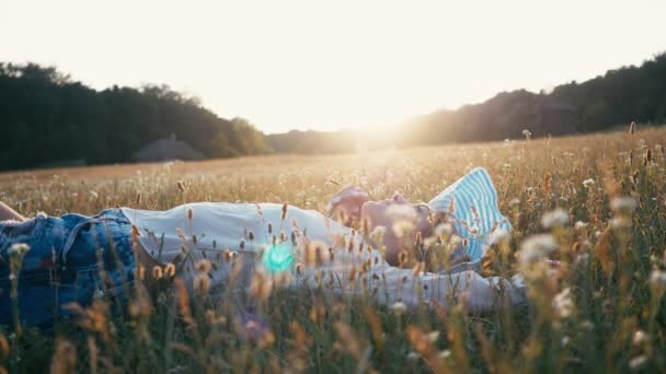 Улыбающаяся красавица лежит на весеннем поле. Мэдоу. Портрет девушки-модели "Смех и счастье" со здоровыми длинными волосами, наслаждающейся природой. Молодая женщина под открытым небом — стоковое видео