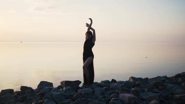 Unbekümmerte Frau im langen schwarzen Kleid tanzt bei Sonnenuntergang am Strand — Stockvideo