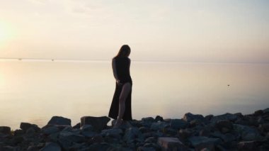 Gün batımında sahilde dans uzun siyah elbiseli kaygısız kadın