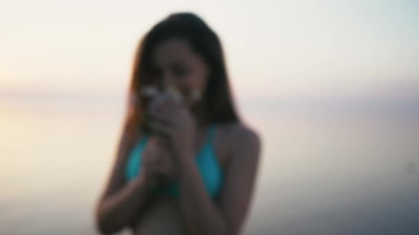 Jonge vrouw staande op de kust en het ruiken van de bloem. Het dragen van bikini en shorts — Stockvideo