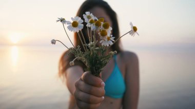 Sahil üzerinde duran ve çiçek kokulu kadın. Bikini ve şort giyiyor