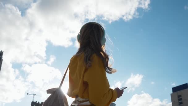 Jolie jeune femme souriante porte des écouteurs écoutant de la musique sur le lecteur de musique à fond flou de la ville. Profiter des airs au ralenti — Video