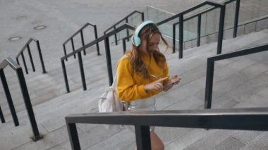 Kentsel şehir sokakları arka planda kulaklık ile müzik dinlemek Genç Sevimli çekici genç kız portresi. Sarı bluz ve gümüş etek giyen kadın