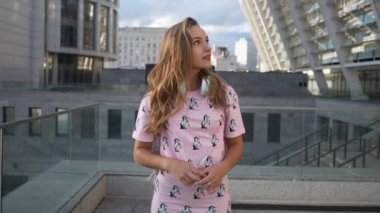 Hareket portre çekici sevimli gülümseyen beyaz elbise genç kadın kentsel ortamda sırt çantası ve kulaklık ile yavaş. Millenial Hipster yeni nesil Y