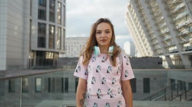 Hareket portre çekici sevimli gülümseyen beyaz elbise genç kadın kentsel ortamda sırt çantası ve kulaklık ile yavaş. Millenial Hipster yeni nesil Y