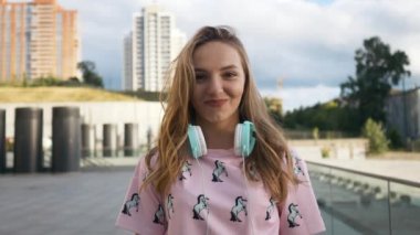 Hareket portre çekici sevimli gülümseyen beyaz elbise genç kadın kentsel ortamda sırt çantası ve kulaklık ile yavaş. Millenial Hipster yeni nesil Y