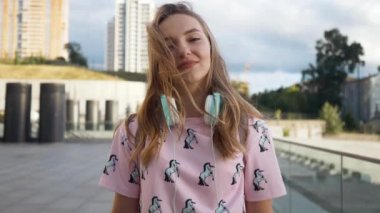 Hareket portre çekici sevimli gülümseyen beyaz elbise genç kadın kentsel ortamda sırt çantası ve kulaklık ile yavaş. Millenial Hipster yeni nesil Y