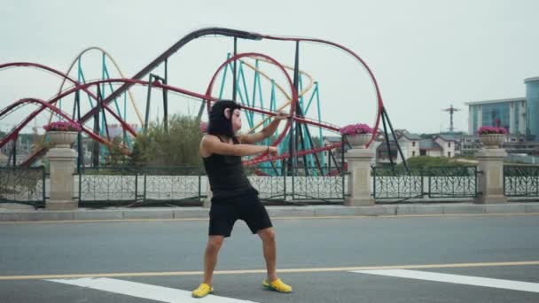 Spaanse man in aap masker dom dansen voor kleurrijke achtbaan in attractiepark met blauwe hemel als achtergrond. Copyspace tekst — Stockvideo