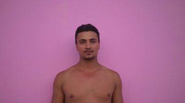 Genç yakışıklı İspanyol adam dikey, çıplak gövde ve bıyık ciddi görünümlü pembe arka plan üzerinde kamera yakın kadar dalgın. Vitiligo deride.