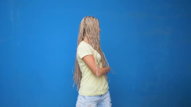 时髦的时髦女孩摇晃她编织的头发辫子和旋转在蓝色背景上 — 图库视频影像