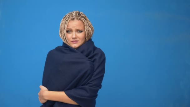 Joven mujer hipster rubia con trenzas en ropa de invierno tratando de calentar sobre fondo azul — Vídeos de Stock