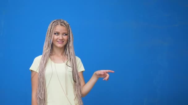 Menina sorridente feliz apontando o dedo para o copyspace e fazendo gesto aprovando isolado sobre fundo azul — Vídeo de Stock