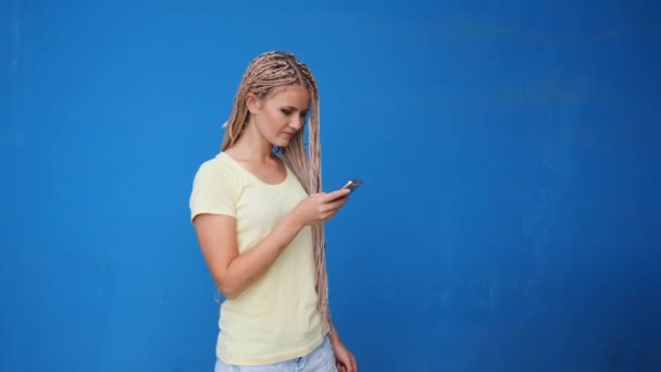 스마트폰 여자 블루 배경 위에 웃 고 전화 통화. 휴대 전화에 캐주얼 대화 데 머리 띠와 아름 다운 젊은 여성 — 비디오