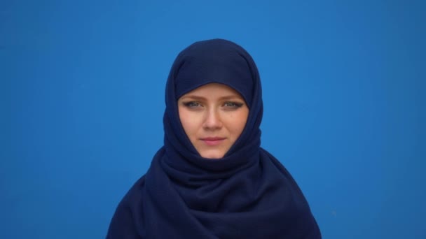 青い背景に野心的な自信の笑みを浮かべて穏やかなプロフェッショナルを探してヒジャーブ スカーフを身に着けている素敵な若いイスラム教徒ビジネス ・ ウーマンの肖像画間近します。 — ストック動画