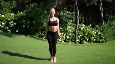 Genç Sarışın kadın zıplattılar fitness egzersiz egzersiz yeşil yaz parkta çayır üzerinde işi örgüler ile. Ağır çekim