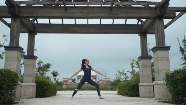 Joven mujer caucásica en ropa deportiva relajándose practicando yoga descalza en el parque de la ciudad. Fondo del amanecer. Movimiento lento — Vídeo de stock