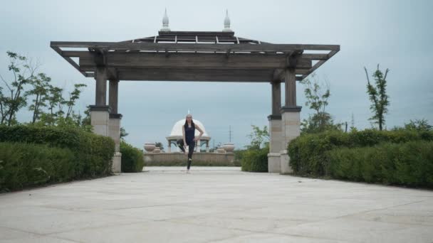 Mulher caucasiana jovem em sportswear relaxante praticando ioga descalço no parque da cidade. Fundo do nascer do sol. Movimento lento — Vídeo de Stock