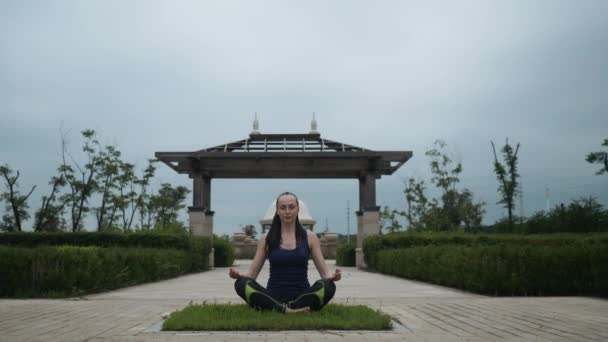 Joven mujer caucásica en ropa deportiva relajándose practicando yoga descalza en el parque de la ciudad. Fondo del amanecer. Movimiento lento — Vídeo de stock