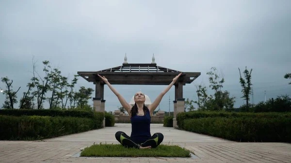 Spor giyim kent parkta yalınayak yoga uygulamak tarafından rahatlatıcı Genç beyaz kadın. Sunrise arka plan. Ağır çekim