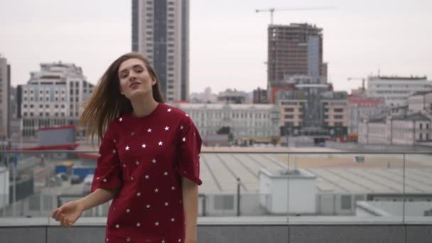 Chica atractiva en un vestido rojo va por la calle en una ciudad — Vídeo de stock