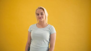 Çekici genç beyaz sarışın artı boyutu modeli kamera sarı arka plan için gülümsemek